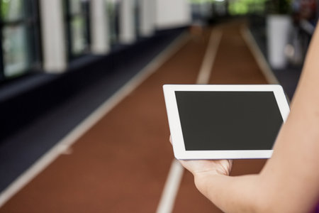 Adult holding tablet and studying track lanes inside sports hall with sunlight filtering. Athlete, digital, modern, fitness, training, interior, energeticの写真素材