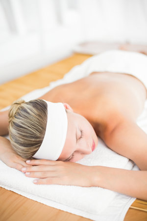 Woman lying face down on wooden-framed massage table in spa room wearing white towel and headband. Serenity, relaxation, health, wellness, therapeutic, skincare, minimalismの写真素材