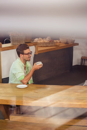 Man wearing casual shirt sitting at cafe bakery holding coffee cup near wicker baskets, copy space. Casual, cozy, rustic, ambient, relaxed, artisan, warmの写真素材