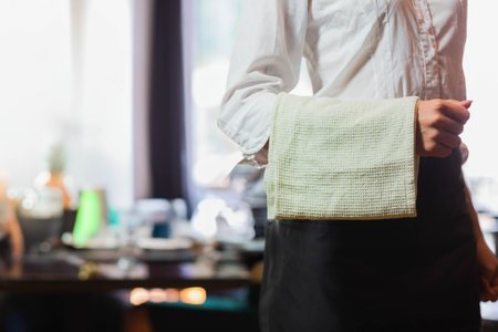 Waffle-weave cloth towel draping over black waist apron in restaurant dining area, with set tables. Hospitality, service, professionalism, neatness, cleanliness, hospitality industry, interior designの写真素材