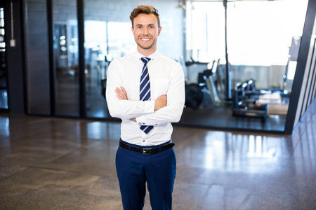 Businessman standing with crossed arms in office gym with glass partitions and exercise bikes. Professional, modern, energetic, motivational, urban, dynamic, sleekの写真素材