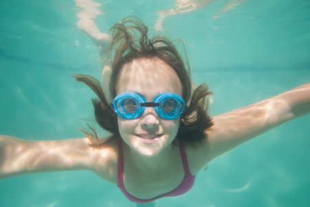Female child swimming underwater in swimming pool wearing blue goggles and pink swimsuit top. Playfulness, adventure, aquatic, childhood, leisure, vibrant, funの写真素材