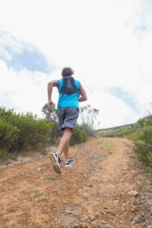 Male athlete ascending steep hillside trail, carrying hydration pack and wearing trail shoes....