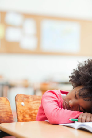 African American girl resting head on book with pencil at desk in classroom, copy space. Learning, concentration, study, education, focus, youth, academicの写真素材