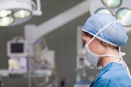 Mid adult female nurse monitoring vitals on monitors under surgical lights in OR, copy space....