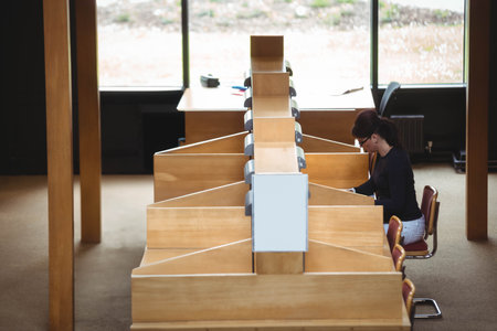 Mid adult female student sitting at wooden study carrel in library typing on laptop, copy space. Concentration, focus, solitude, academic, innovation, productivity, modernの写真素材