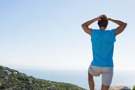 Man standing on ridge wearing blue sportswear gazing at sea horizon under clear sky, copy space....