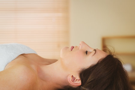 Woman receiving acupuncture needle on cushioned spa table draped white towel under wooden blinds. Wellness, relaxation, holistic, tranquility, therapy, natural, comfortの写真素材