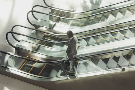 Glass-and-metal escalators moving in modern office atrium under soft light, with plant shadows. Urban, architecture, contemporary, corporate, minimalist, professional, reflectiveの写真素材
