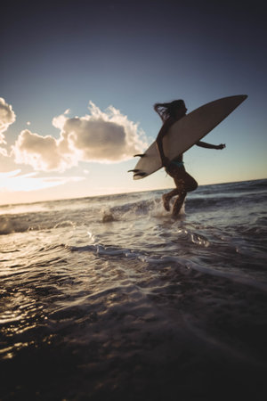 Long white surfboard in the ocean as warm sunset light sparkling on wet sand. Adventure, coastal, vibrant, dynamic, tranquility, leisure, outdoorの写真素材