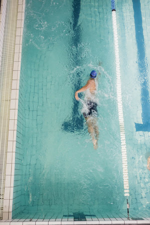 Male swimmer performing freestyle stroke in lane with white and blue divider, creating ripples....