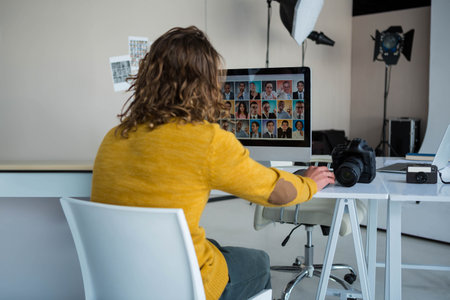 Widescreen monitor displaying headshot grid on desk in studio, with DSLR and compact cameras. Studio, photographer, editing, professional, workspace, equipment, lightingの写真素材