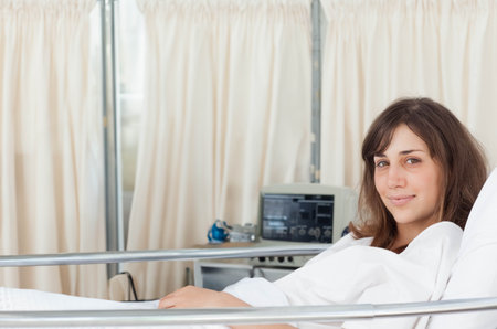 Woman patient reclining in hospital bed with metal rail beside vital signs monitor, copy space. Medical, healthcare, relaxation, clinical, patient care, wellness, hospital environmentの写真素材