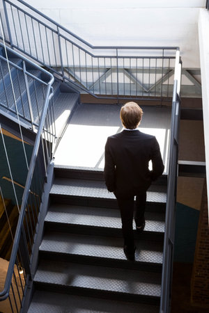 Business male ascending steel staircase with handrails in industrial stairwell lighting white walls....