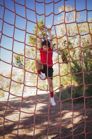 School-aged boy climbing red rope net on obstacle course wearing sweat wristband, white shoes. Adventure, youth, outdoor, athleticism, nature, challenge, explorationの写真素材