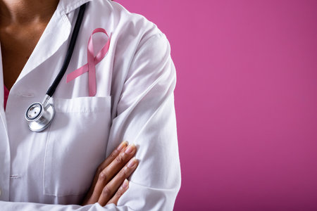 Midsection of african american mid adult doctor with pink breast cancer awareness ribbon, copy space. pink background, doctor, medical, awareness, support, healthcare and medical occupation.の写真素材