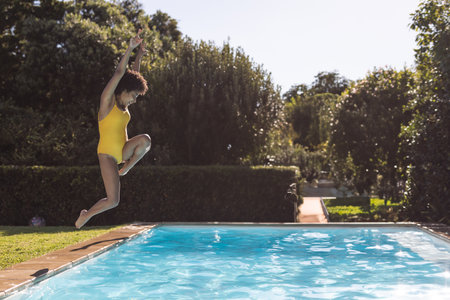 African American woman leaping at pool edge in backyard with blue water, copy space. Vibrant,...