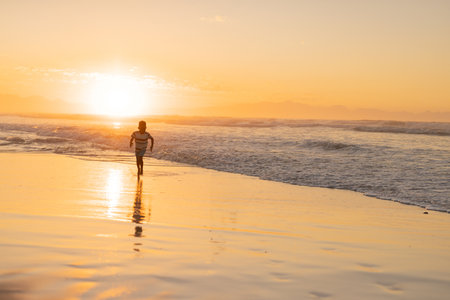 African American boy running at sunset on wet beach sand, waves lapping and sun reflecting. Seascape, childhood, exploration, leisure, tranquility, adventure, outdoorの写真素材