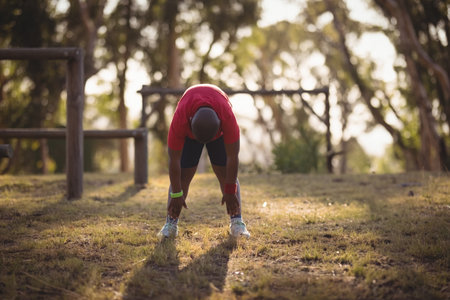 lone man bending and stretching legs wearing fitness tracker near wooden bars in grassy park. Outdoor fitness, wellness, athletic, nature, activewear, health, exerciseの写真素材