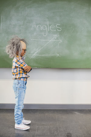 African American boy wearing gray wig crossing arms facing classroom chalkboard angle, copy space. Education, student, classroom, learning, geometry, teaching, academicの写真素材