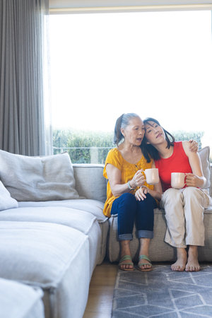 Sitting Asian family sharing warm drinks in cozy living room, with white mugs, copy space. Family, bonding, warmth, affection, companionship, interior, modernの写真素材