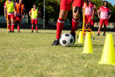 Low section of multiracial male player kicking ball between cones while practicing soccer. Soccer...