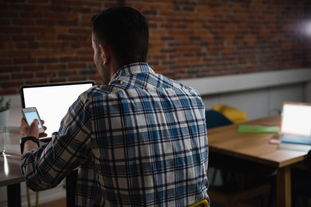 Man using smartphone and blank-screen laptop at wooden desk with potted plant, copy space. Professional, workspace, rustic, modern, productivity, entrepreneurship, interiorの写真素材
