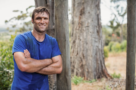 mature man leaning on wooden post amid tree trunks and dry-grass, wearing blue T-shirt, copy space. Farmer, outdoors, countryside, rural, nature, overcast, calmの写真素材