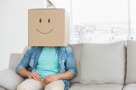 Adult male sitting on light-gray sofa in living room by window wearing denim shirt. Anonymous, urban, daylight, minimalist, contemporary, playful, interiorの写真素材
