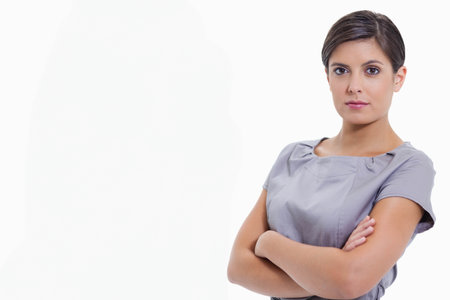 Woman standing with arms folded, facing camera in white studio wearing grey dress, copy space. Headshot, corporate, professional, executive, confident, minimal, cleanの写真素材