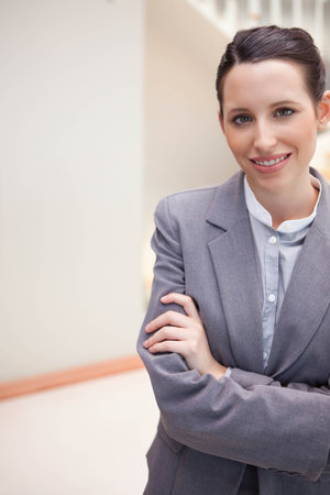 Female professional standing in office corridor wearing grey blazer and light shirt, copy space. Executive, attire, hallway, reception, polished, corporateの写真素材