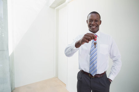African American man holding red key fob and keys, wearing shirt and striped tie, copy space. Professional, corporate, interior, daylight, entryway, bright, modernの写真素材