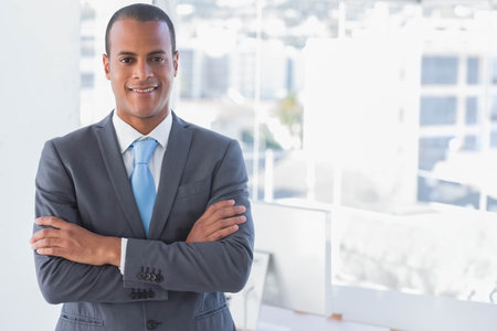 African American man wearing gray suit tie standing arms crossed by office windows, copy space. Executive, headshot, corporate, professional, cityview, skyline, modernの写真素材
