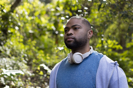 African American man wearing hoodie and headphones standing amid lush forest, copy space. Nature, serenity, outdoor, leisure, greenery, tranquility, wildernessの写真素材