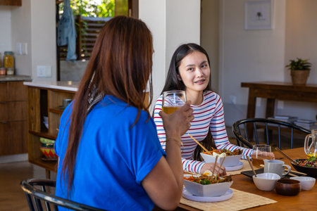 Asian mother and daughter sharing casual meal at home dining table with bowls and chopsticks. Family, cuisine, rustic, cozy, bonding, comfort, atmosphereの写真素材