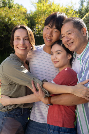 Asian family hugging in backyard garden under bright sunlight with lush green shrubs and trees. Family, togetherness, outdoor, nature, happiness, camaraderie, vibrantの写真素材