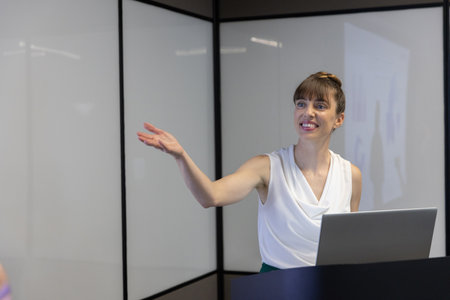 Woman presenting at podium using laptop in glass partitioned conference room, copy space. Speaker,...