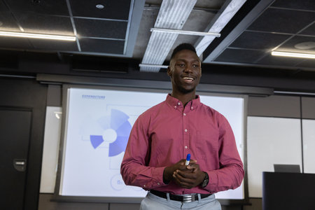African American man holding blue marker presenting pie chart on projection screen in meeting room....