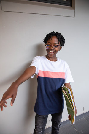 Teen African American male standing in school hallway holding notebooks in color-block tee smiling....