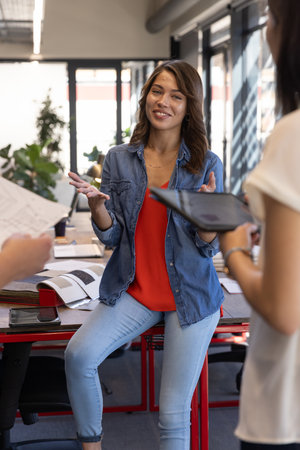 Diverse coworkers leaning on table discussing ideas in open-plan office with documents and tablet....