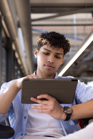 African American man wearing watch holding tablet and sitting on armrest chair at coworking desk....