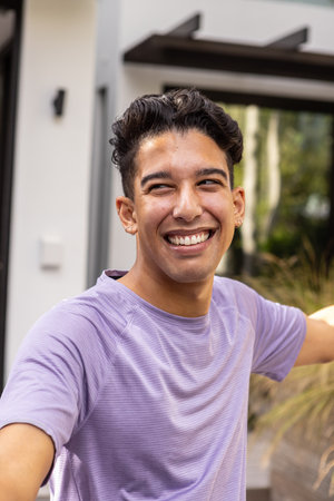 Man wearing purple athletic shirt smiling and stretching arms outside modern home near grasses....