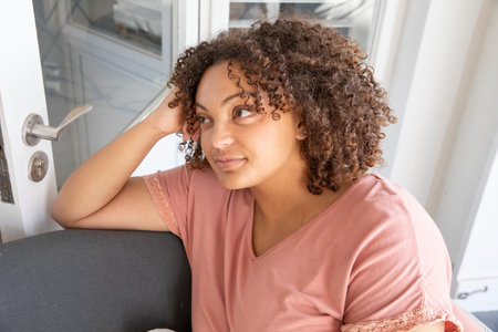 African American woman resting elbow on padded chair inside room near frosted glass door panels....