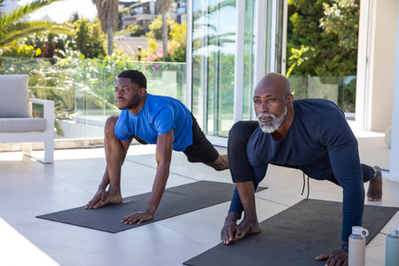 African American father and son performing lunges on black yoga mats on home terrace. Outdoor,...