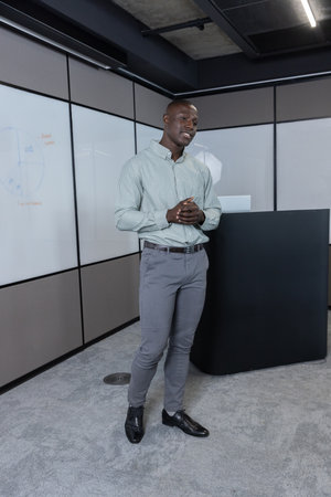 African American man presenting data on laptop beside podium and whiteboards in conference room....