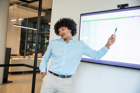 African American man presenting spreadsheet on screen in office holding marker leaning against wall. Business, presentation, modern, professional, workspace, analysis, communicationの写真素材