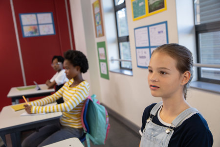 Diverse classmates sitting at desks in classroom using pencils and typing on laptop, copy space....
