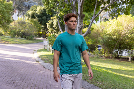 Fair-skinned man walking along brick-paved path through suburban green space past signpost. Outdoor, leisure, landscape, lifestyle, nature, stroll, serenityの写真素材