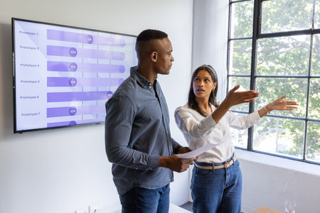 Diverse coworkers reviewing chart on screen while holding report in office with glass of water....