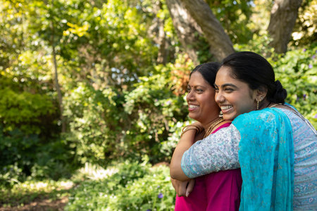 Indian mother and daughter standing in sunlit garden hugging in kurtas and jewelry, copy space. Family, bonding, tradition, nature, serenity, happiness, vibrantの写真素材